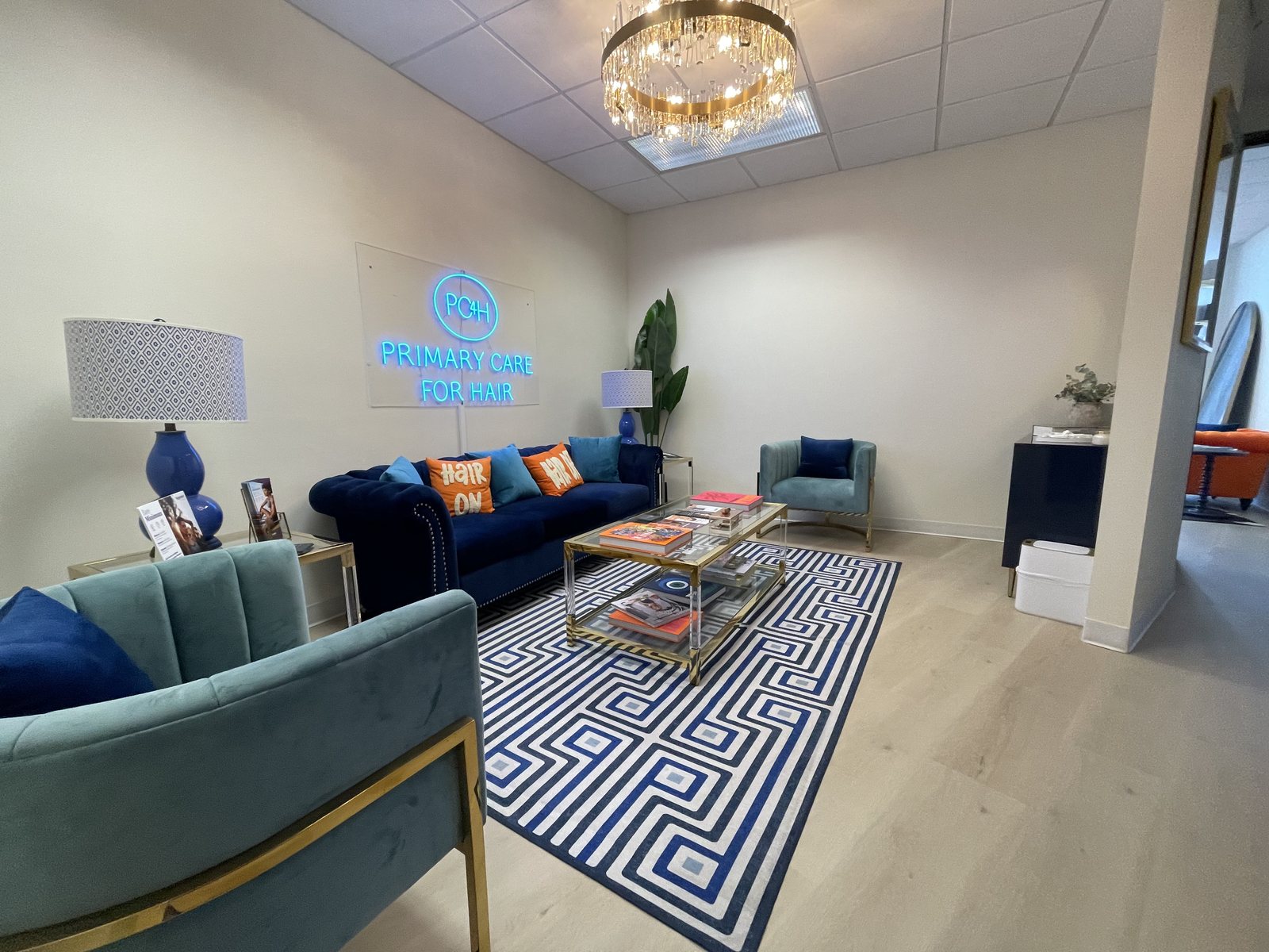 The Primary Care 4 Hair reception lounge in Newport Beach, with navy and teal velvet seating and the PC4H sign on the wall